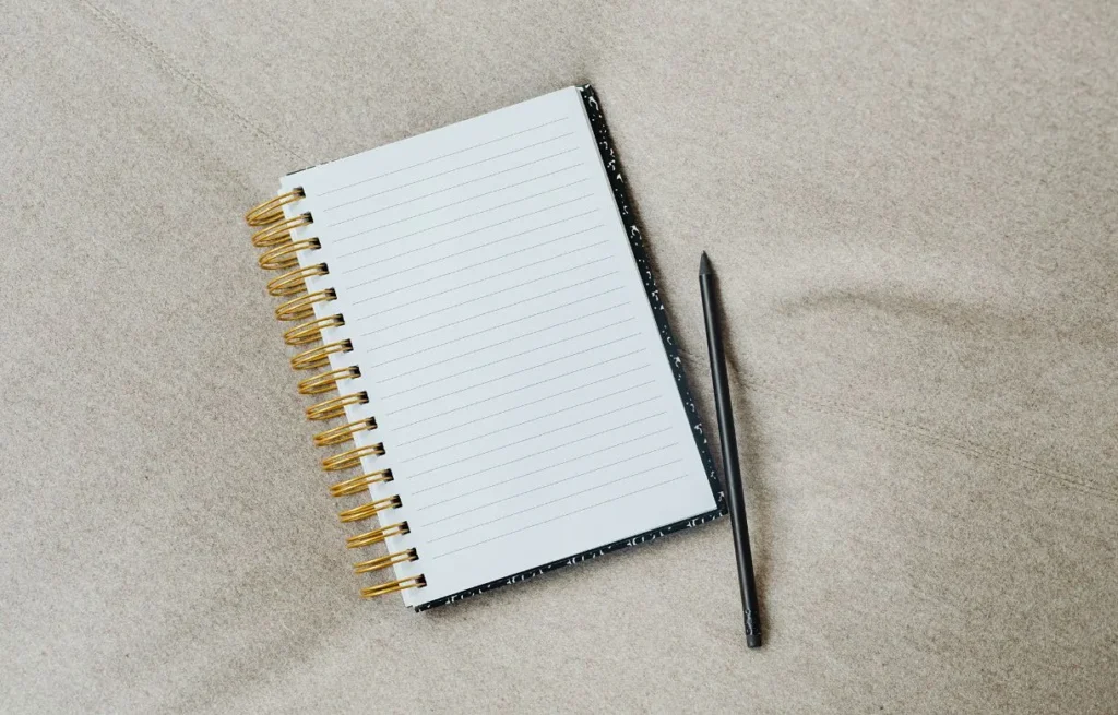 Carnet ligné ouvert et crayon posés sur une surface claire, pour les exercices d'écriture du guide